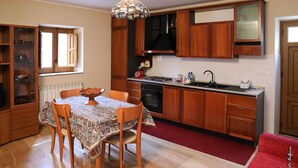 Una cocina compacta con armarios de madera, una mesa de comedor con sillas, una alfombra roja y una lámpara colgante.