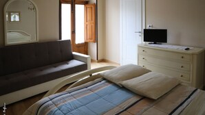 Un dormitorio con cama, sofá, cómoda, televisor y una puerta que da a otra habitación.