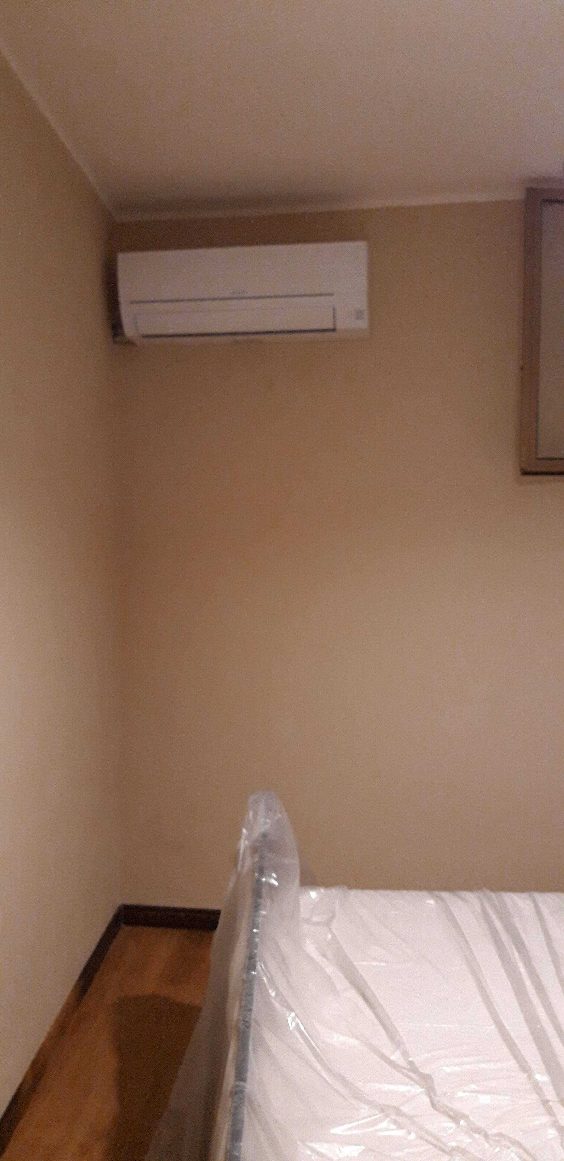 Ein Zimmer mit einem mit Plastik bezogenen Bett, einer Wandklimaanlage und einem Holzboden.