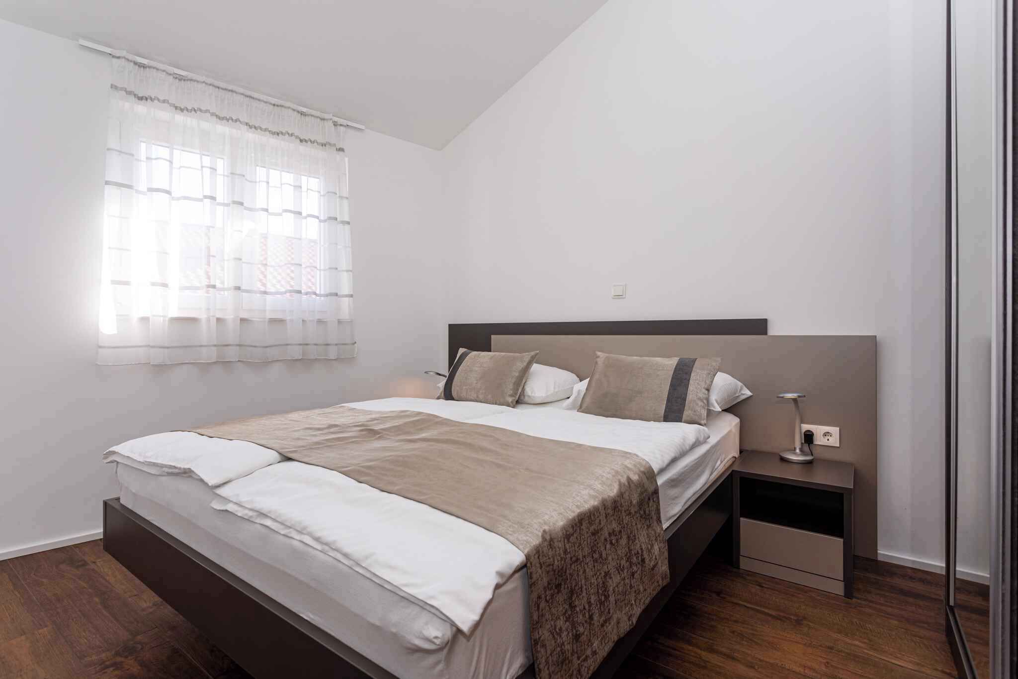 A modern bedroom with a large bed, a nightstand, and a window with sheer curtains.