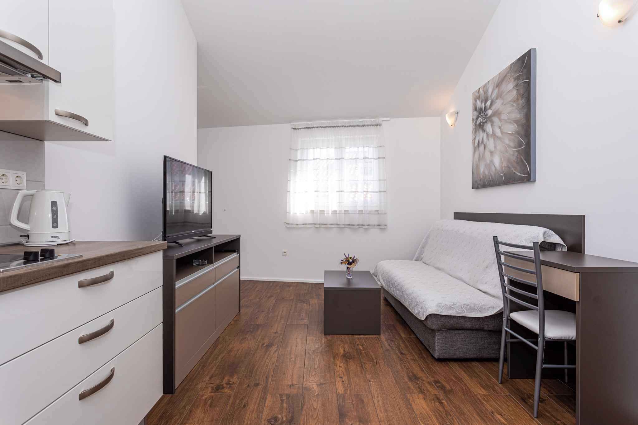 Una habitación compacta con kitchenette, una cama, una pequeña mesa y una silla.