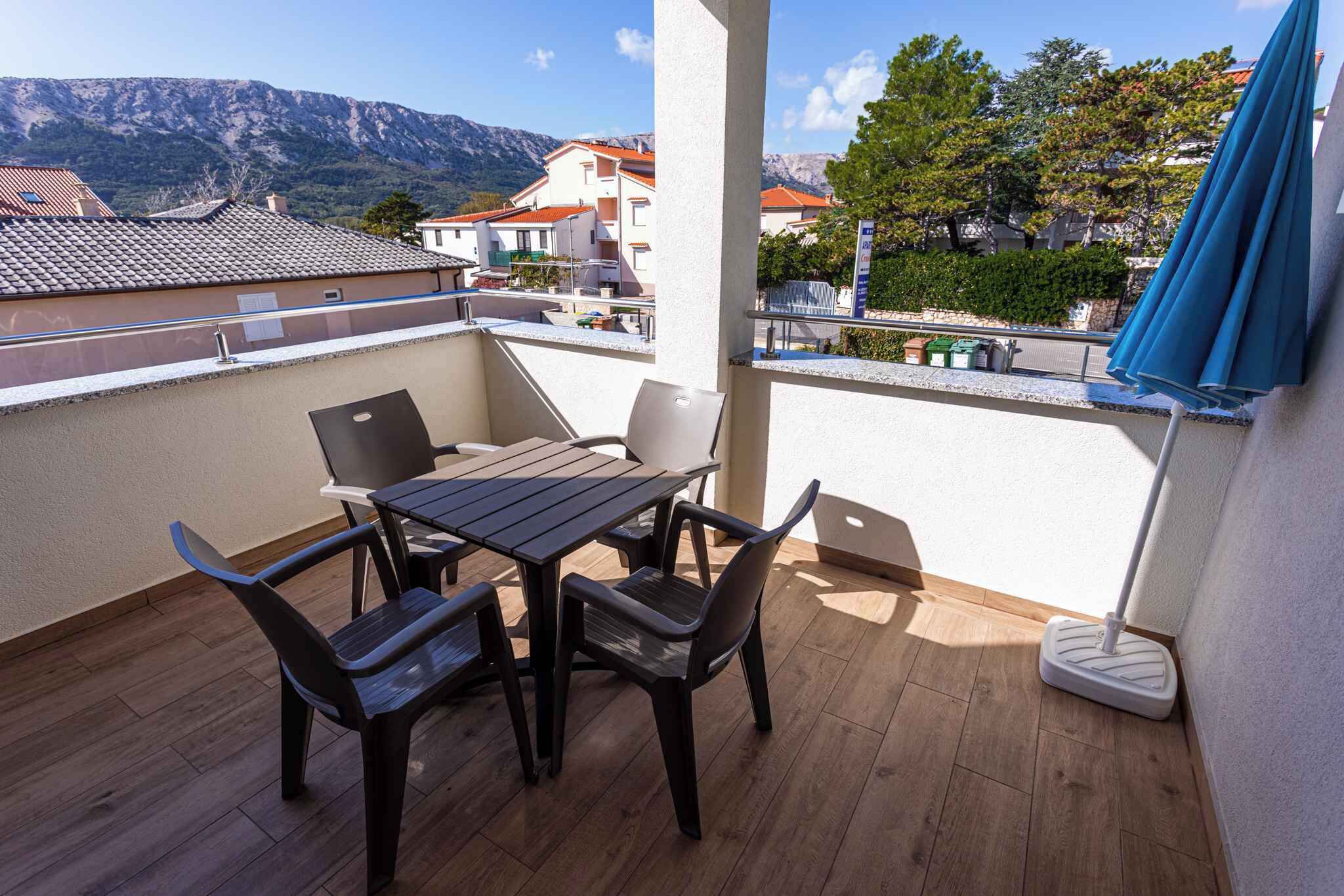 A balcony with a table and chairs, a mop, and a view of buildings and mountains.