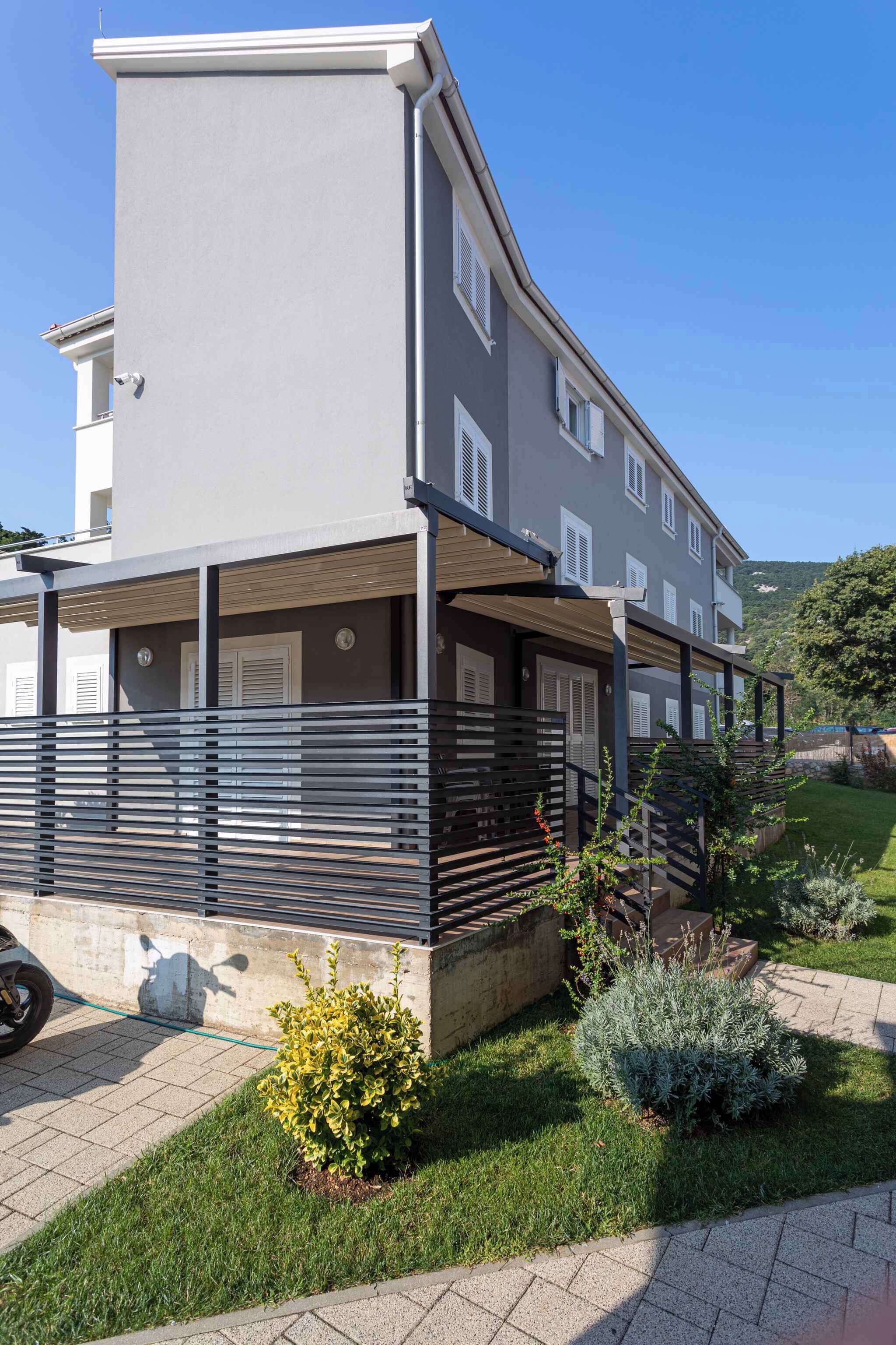 A modern multi-story residential building with a covered outdoor area, a paved driveway, and well-maintained landscaping.