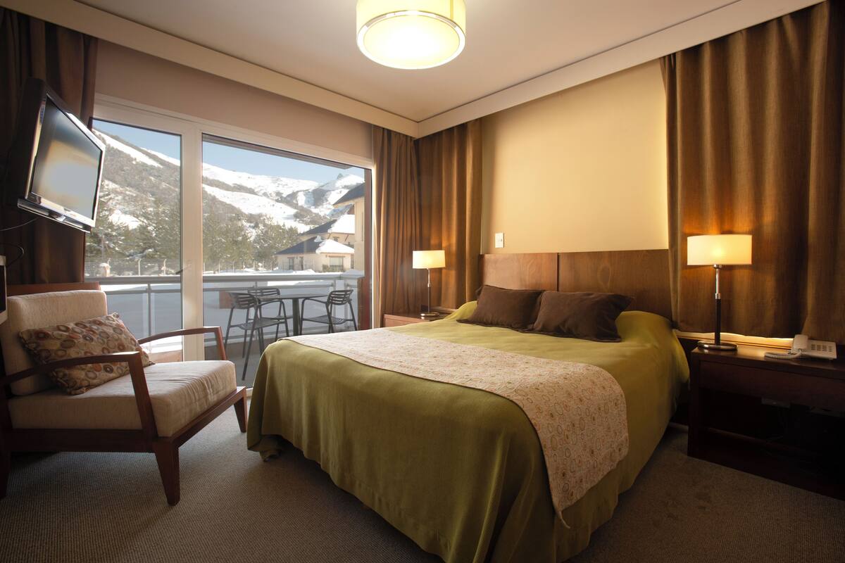 Ein Hotelzimmer mit einem Bett, einem Sessel, einem Schreibtisch und einem Fernseher.