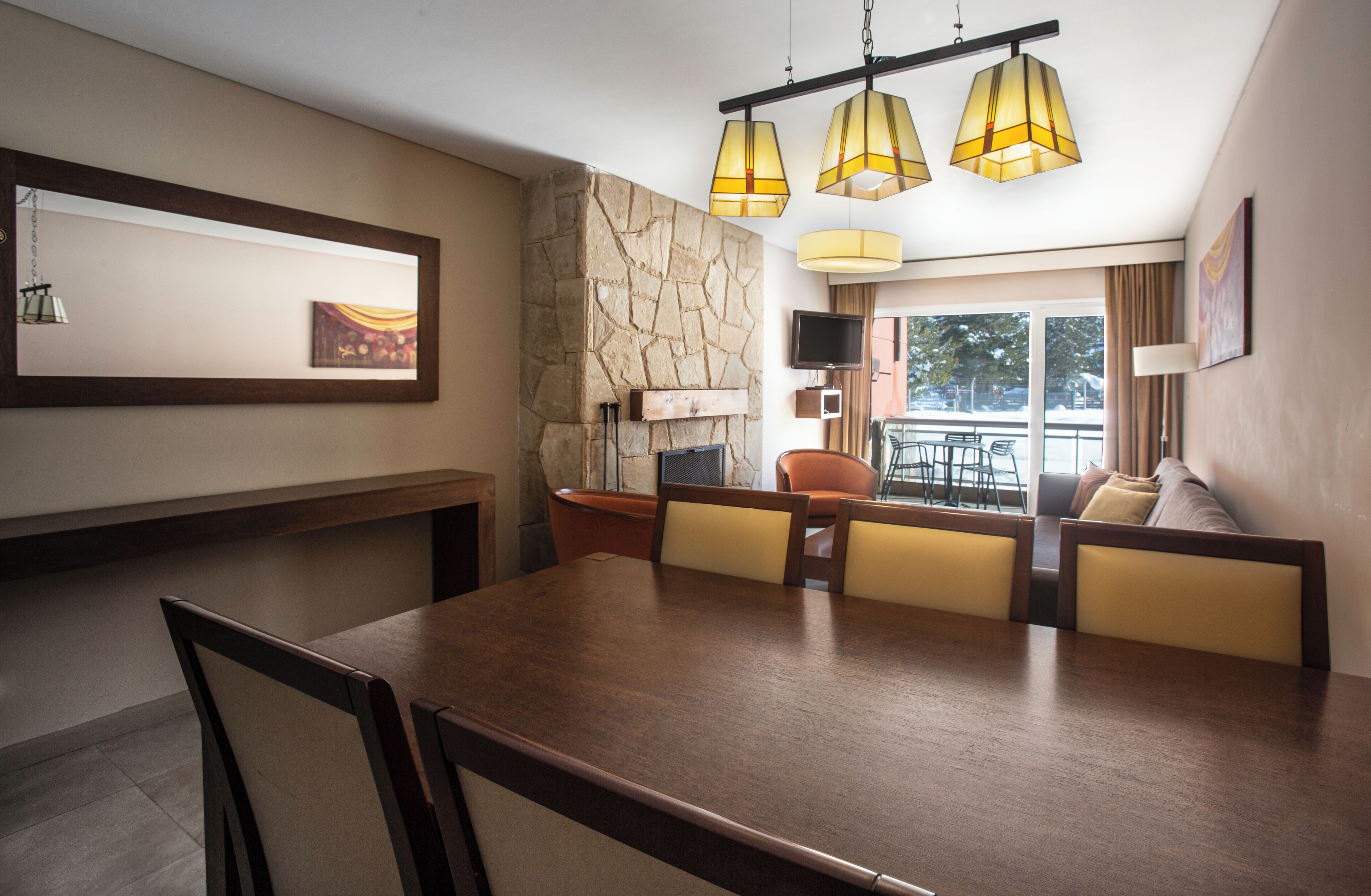 A dining area with a wooden table and chairs, a stone accent wall, and a view of the outdoors.
