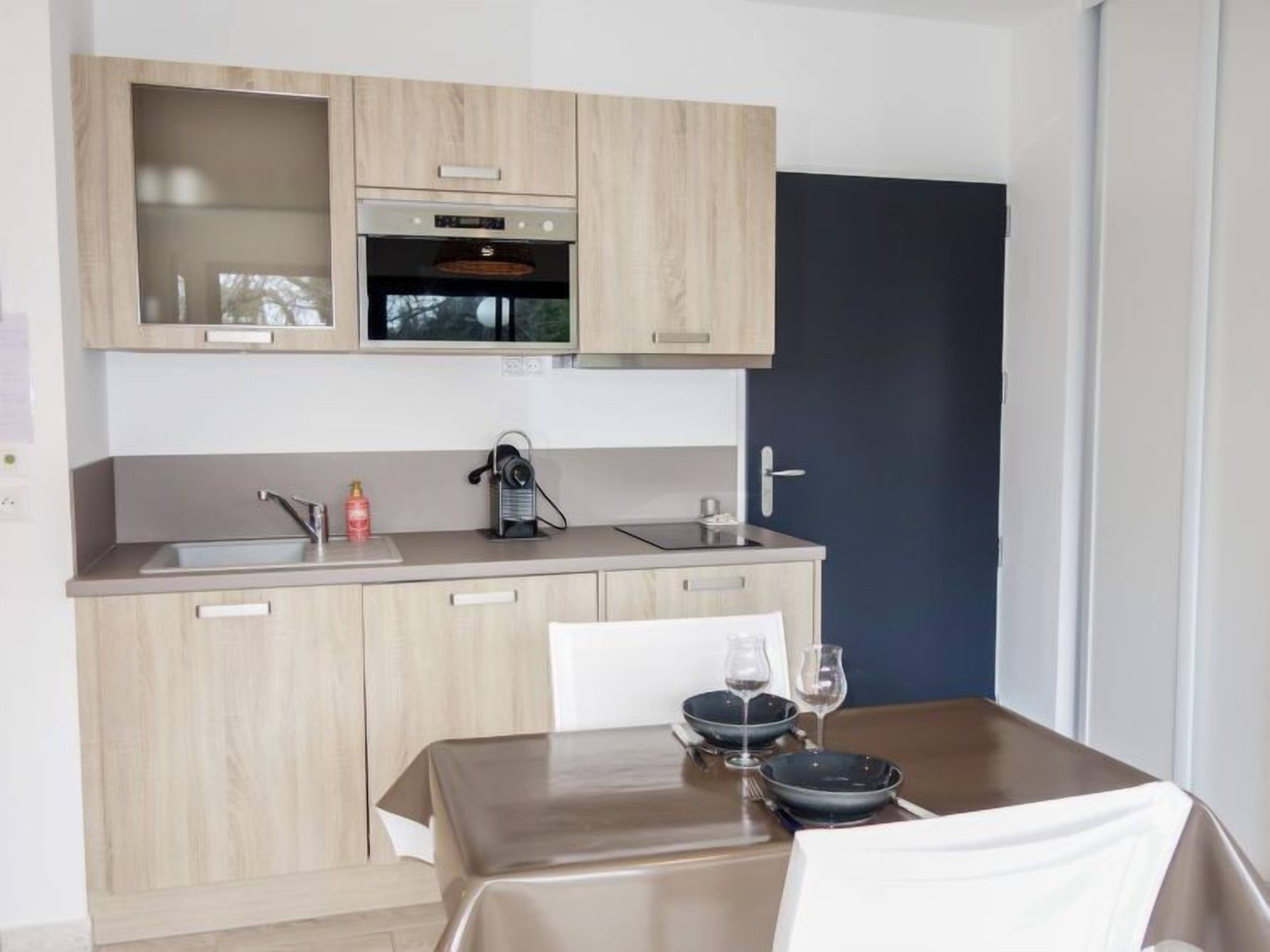 A modern kitchen with light wood cabinetry, a built-in oven, and a dining area with a table set for two.