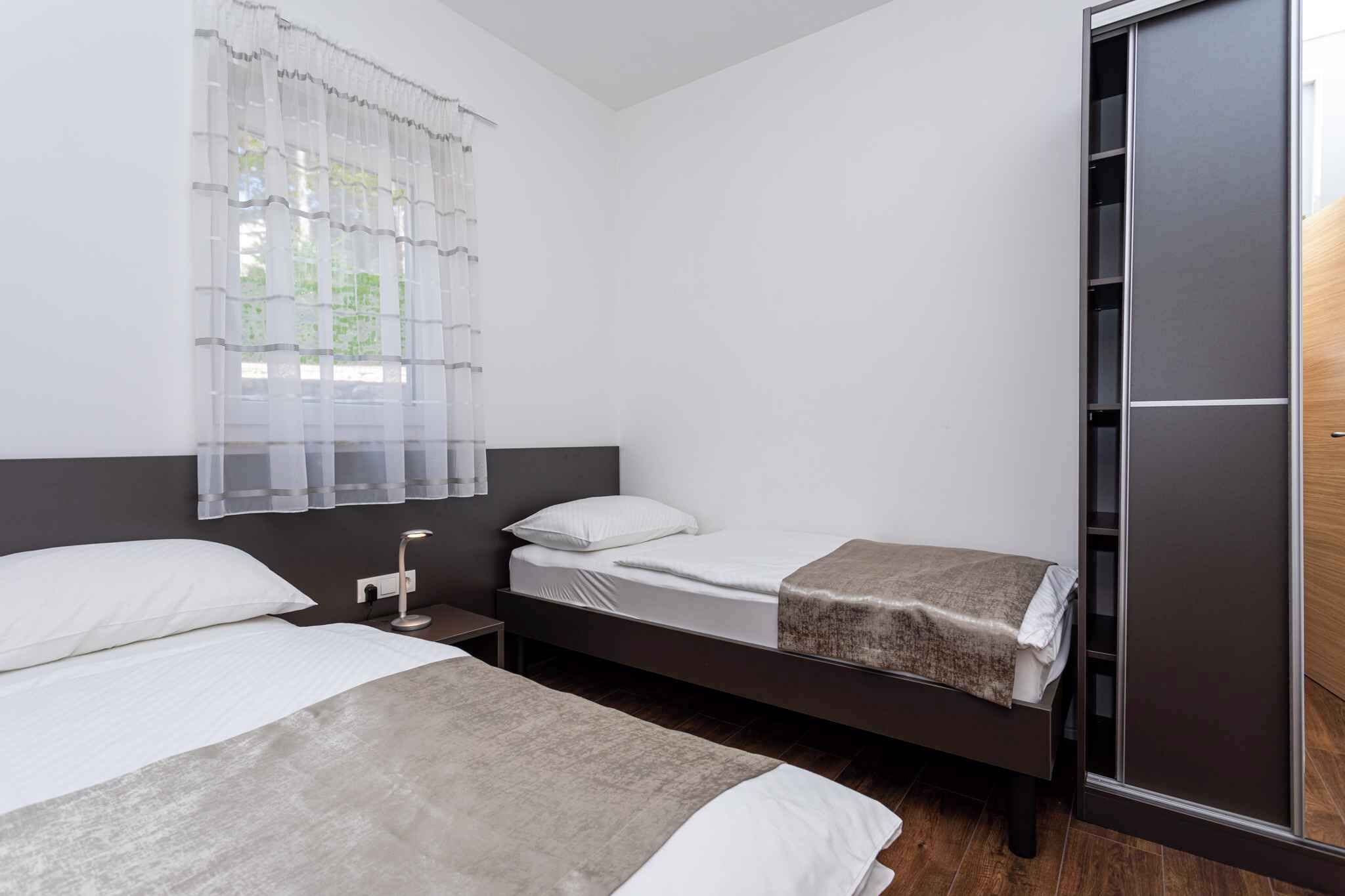 A modern hotel room with two beds, a large wardrobe, and a window with sheer curtains.