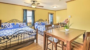 Une chambre avec deux lits, une table à manger, des chaises, un ventilateur de plafond et une plante en pot.