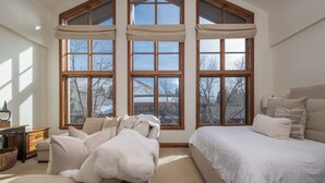 Ein Schlafzimmer mit großem Fenster, einem Bett, einer Couch und einem Nachttisch.