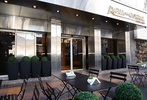 Et udendørs siddeområde med borde og stole foran en hotels indgang.