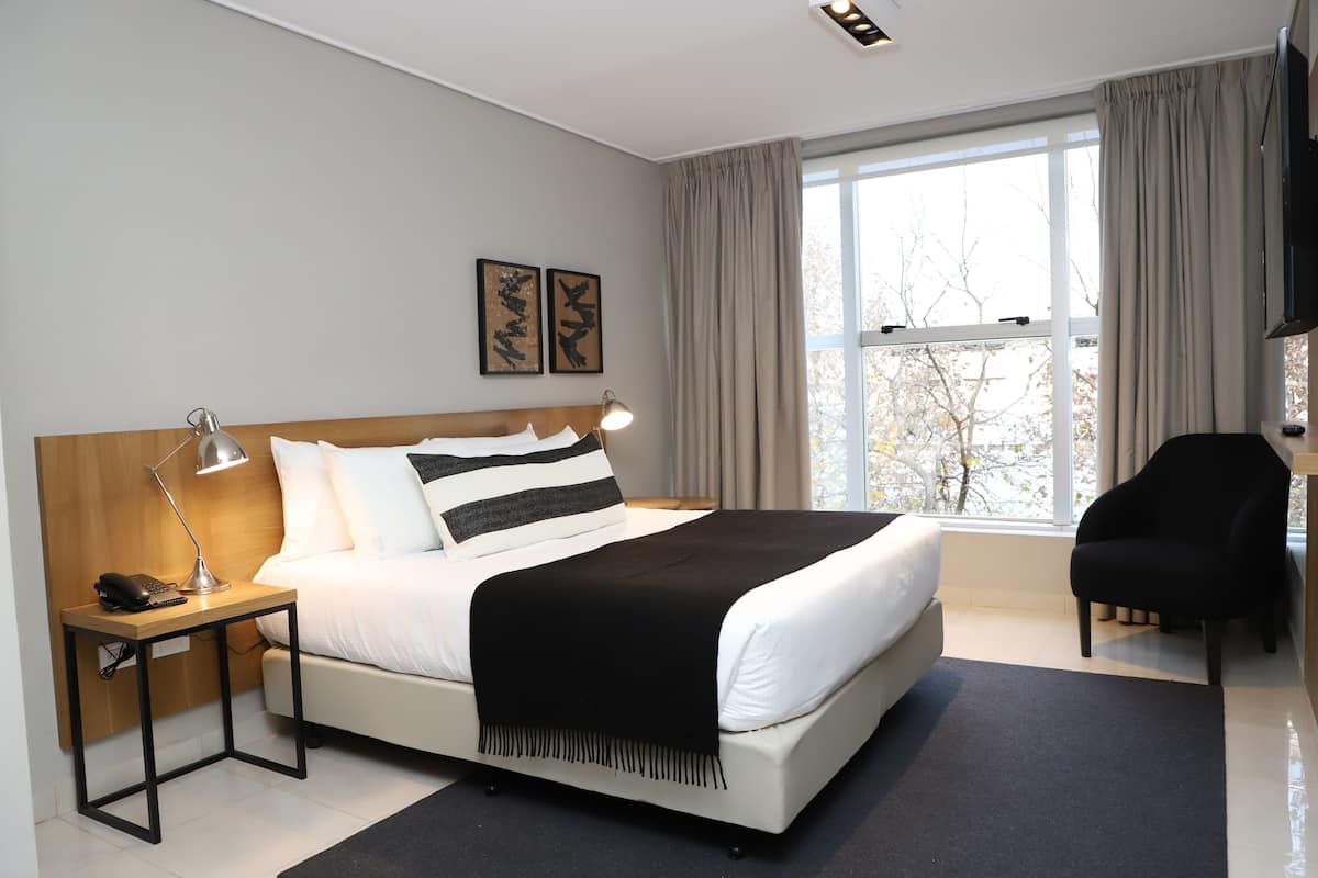 Ett modernt hotellrum med en stor säng, ett nattduksbord med en lampa, en stol och en tv.