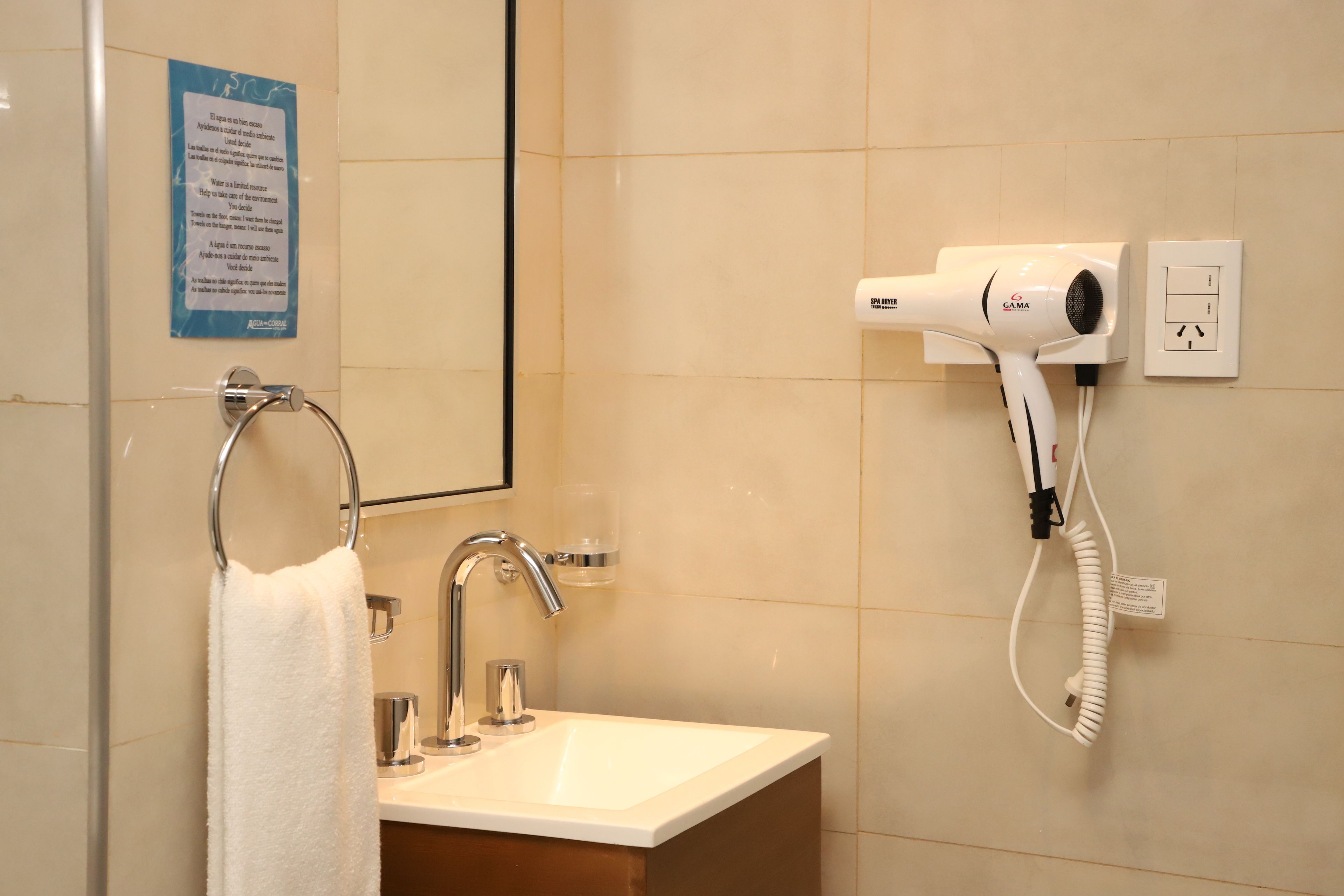 A bathroom with a sink, a towel rack, a mirror, a hairdryer, and a wall-mounted electrical outlet.