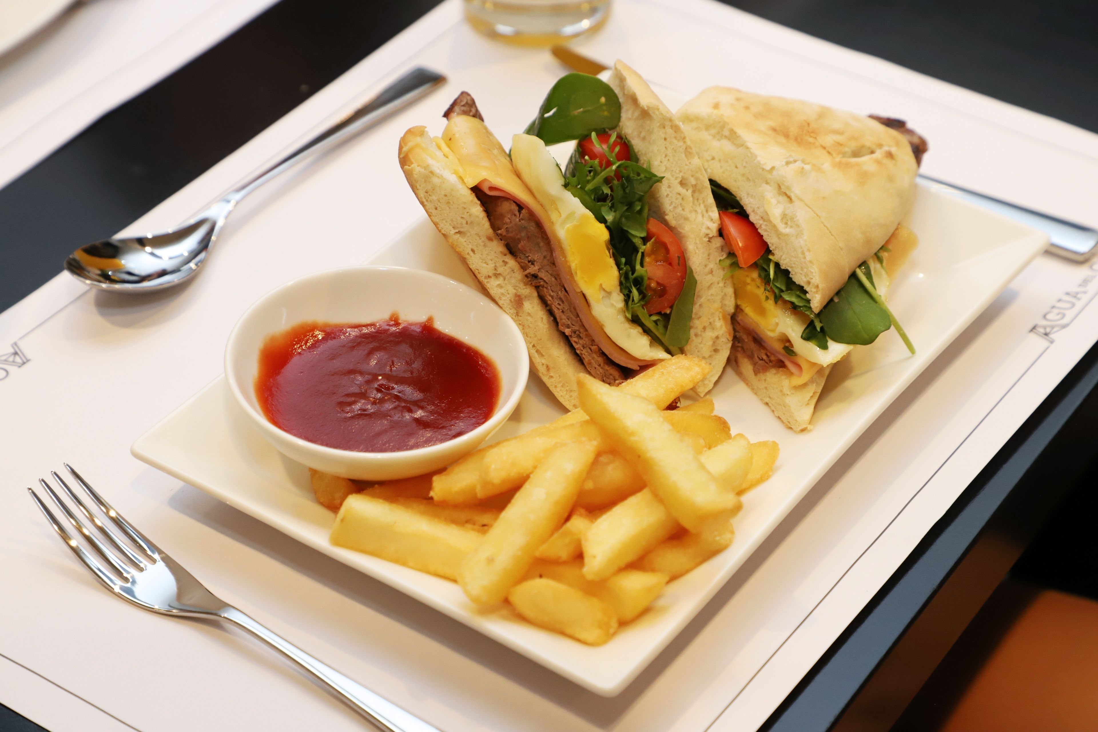 A sandwich with fries and ketchup on a white plate.