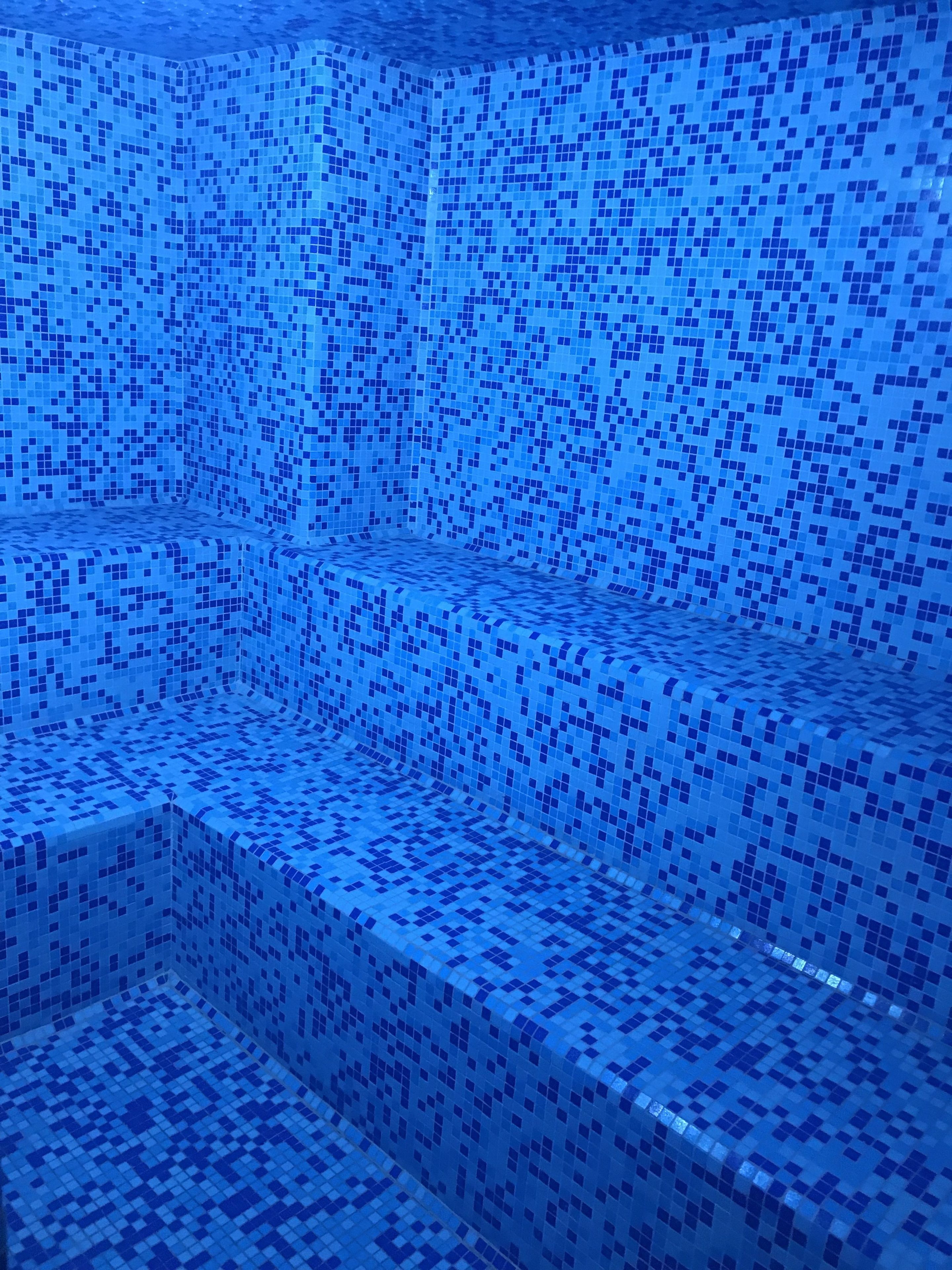 Una piscina con piso y paredes cubiertas de baldosas, rodeada por un borde de azulejos azules.