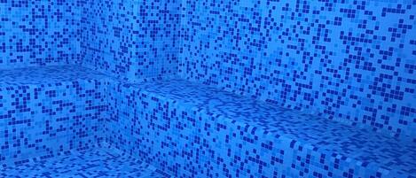 Una piscina con piso y paredes cubiertas de baldosas, rodeada por un borde de azulejos azules.