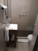 Et badeværelse med hvid vask, hårtørrer, håndklædetørrestativ og toilet.