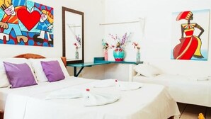 Habitación de hotel con dos camas, una mesita con un florero y cuadros en las paredes.