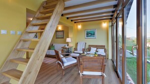 Ein Zimmer mit einer Holztreppe, einem Esstisch mit Stühlen, einer Couch und einem Fenster mit Blick auf Grünflächen.