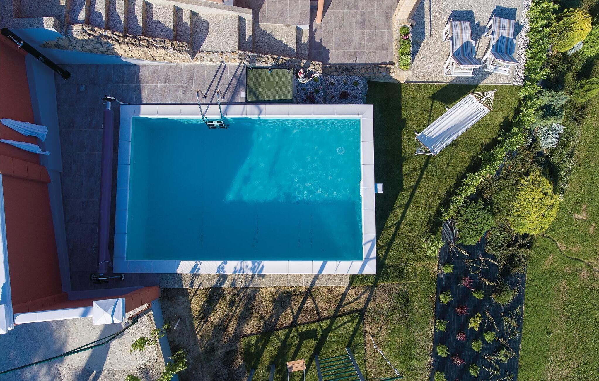 Vue aérienne d’une piscine avec un plongeoir, entourée d’une pelouse bien entretenue et de quelques chaises longues.