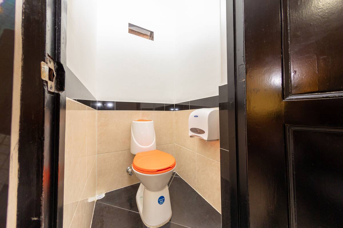 Een kleine, moderne badkamer met een wit toilet, een oranje deksel en een handdroger.