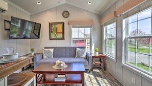 A spacious living room with a grey sofa, a wooden coffee table, and a TV mounted on the wall. There is a large window providing a view of the outdoors. - Equestrian House- Dosanko Cottage (Pleasant Mount)