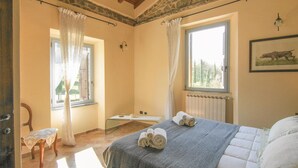 Een slaapkamer met een bed, raam, verwarming en een stoel.