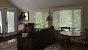 A living room with a sofa, a dining table with chairs, and large windows with blinds. - Walk everywhere in the adorable village of Suttons Bay. (SUTTONS BAY)