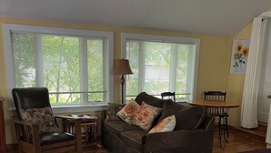A room with a bed, a sofa, a chair, a table, and a lamp. There are windows with blinds and a painting on the wall. - Walk everywhere in the adorable village of Suttons Bay. (SUTTONS BAY)