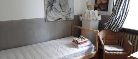 Una habitación pequeña con una cama individual, cabecera de madera, una silla y un radiador.