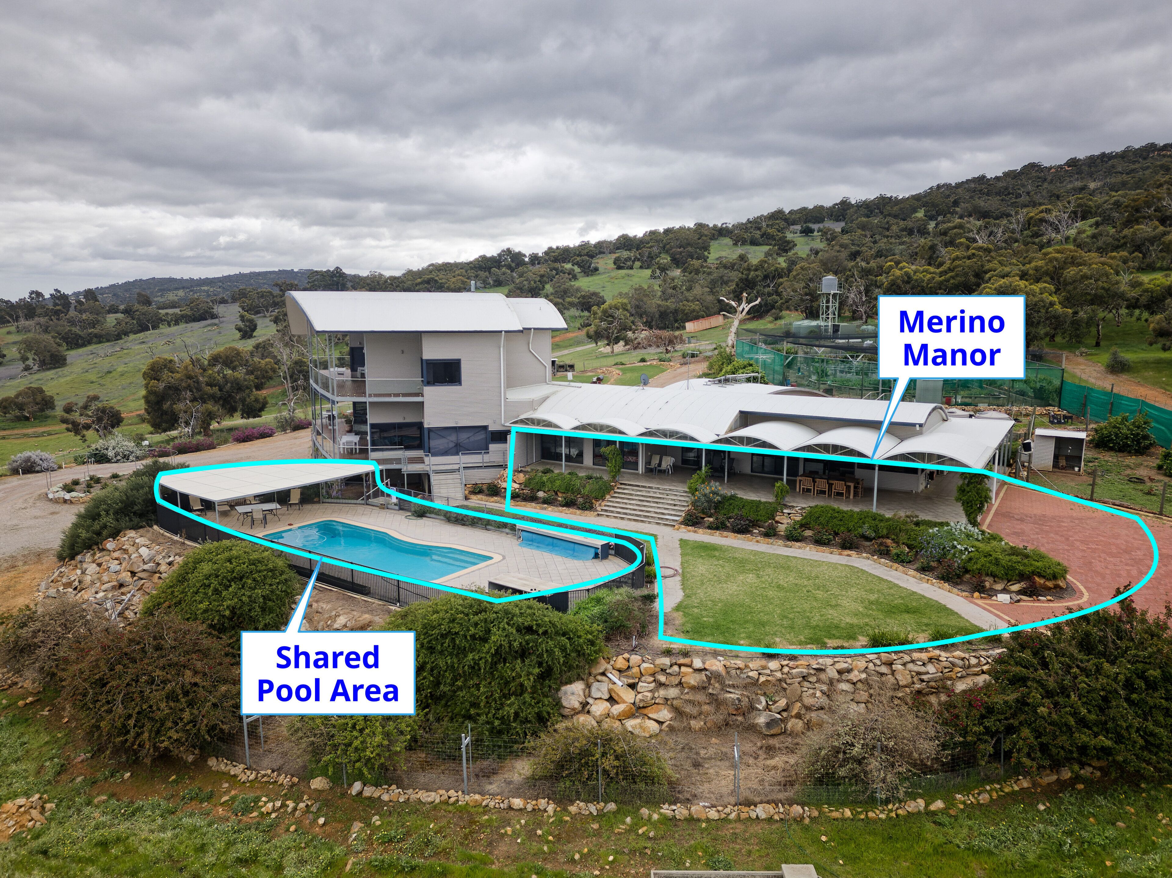 A modern two-story house with a large pool area and a tennis court, surrounded by lush greenery and hills.