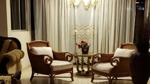 A room with a polished floor, two wooden armchairs, a small round table with a vase of flowers, and a large vase on the right. - Spacious & Comfortable Penthouse in DR (Santo Domingo)