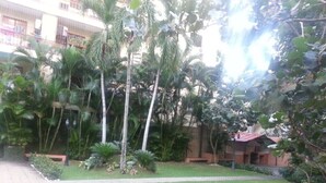 A courtyard with palm trees, a grassy area, and a building with a red roof. - Spacious & Comfortable Penthouse in DR (Santo Domingo)