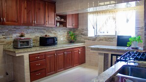 A kitchen with wooden cabinets, a stone backsplash, a microwave, a toaster, and a sink. - Spacious & Comfortable Penthouse in DR (Santo Domingo)