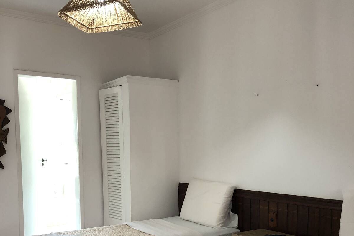 Hotellihuone, jossa on kaksi sänkyä, vaatekaappi, yöpöytä ja riippuvalaisin.