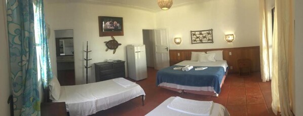 Une chambre d’hôtel avec deux lits simples, un bureau avec une chaise, un réfrigérateur et un téléviseur fixé au mur.