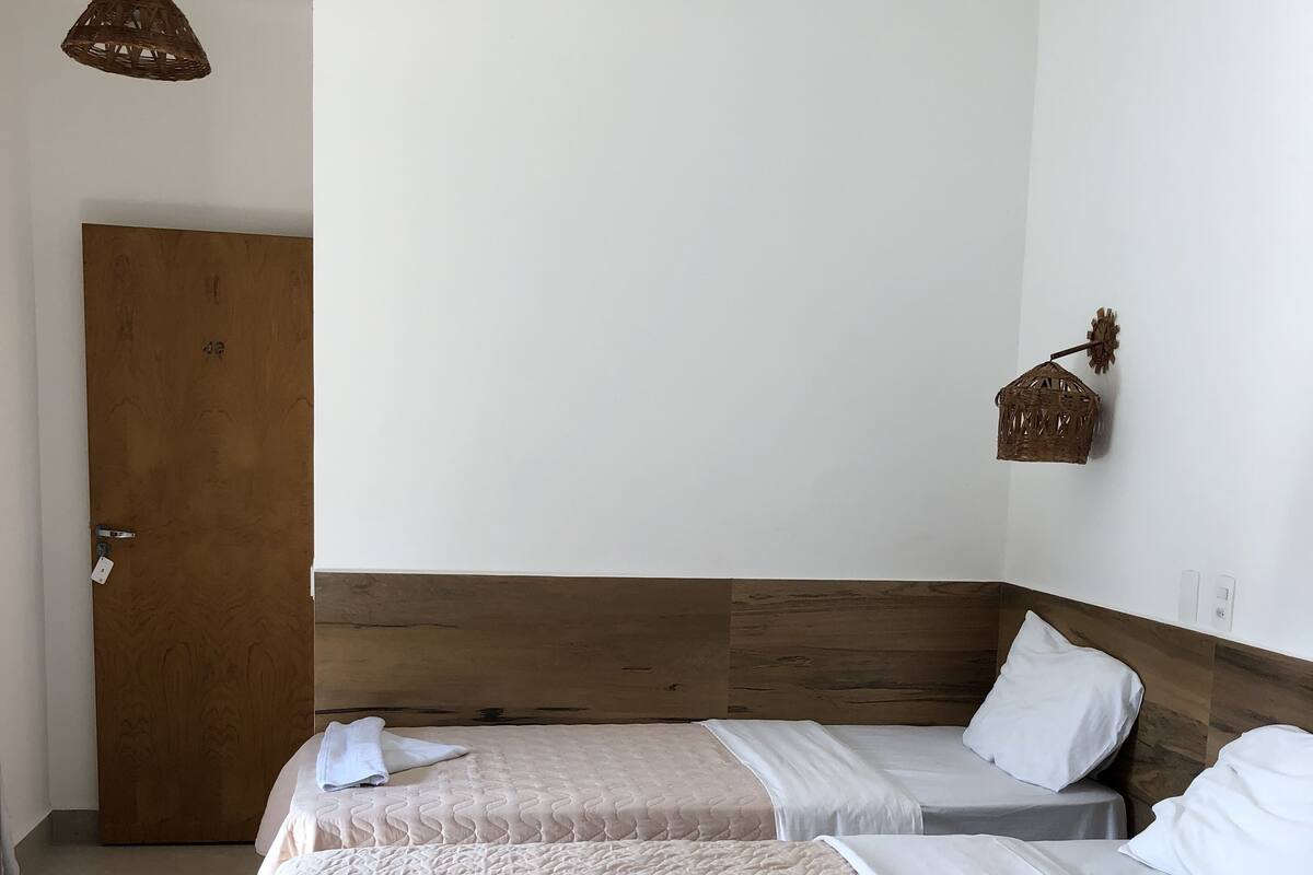 Hotellihuone, jossa on kaksi sänkyä, puinen pääty ja ovi sekä seinään kiinnitetty valaisin.