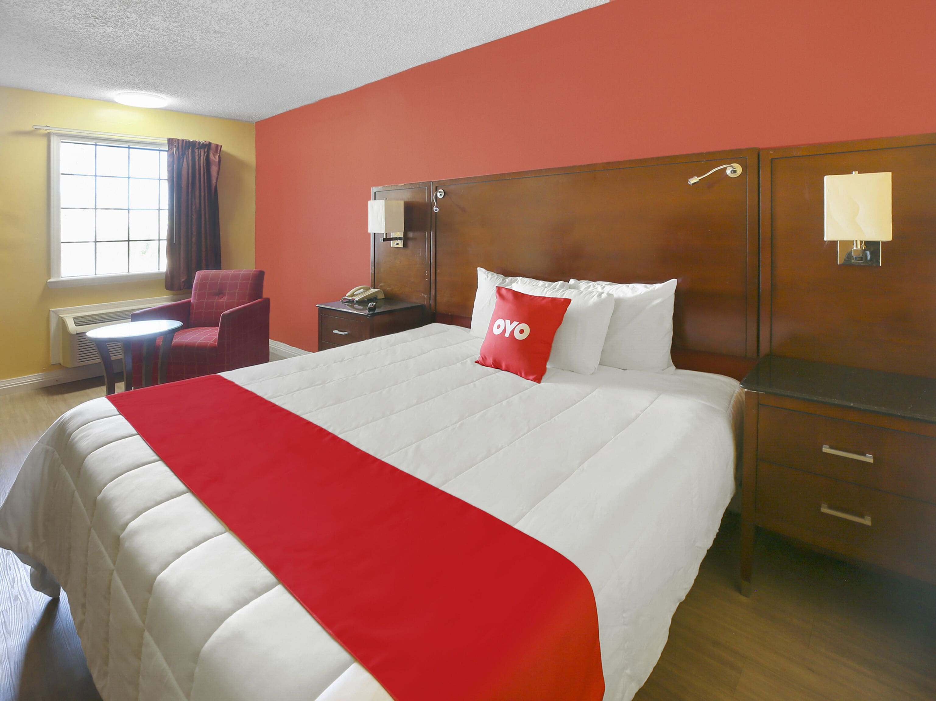 A hotel room with a large bed, a desk, a chair, a nightstand, and a window with curtains.