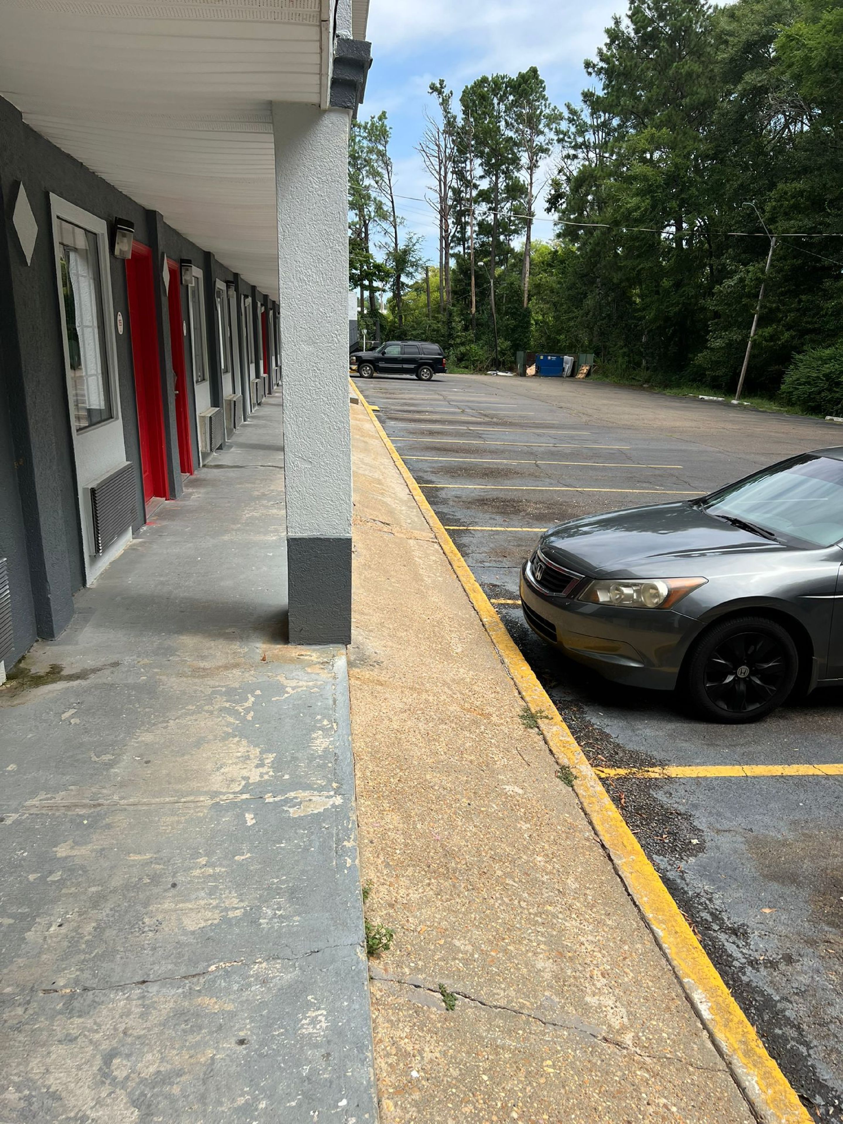 Un estacionamiento con una hilera de edificios, un coche aparcado y una grieta visible en el pavimento.