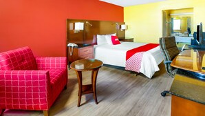 Una habitación de hotel con cama, escritorio, silla, mesita pequeña y mesita de noche.