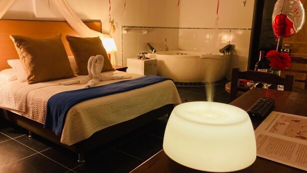 Habitación de hotel con cama, mesita de noche, lámpara y baño con bañera.