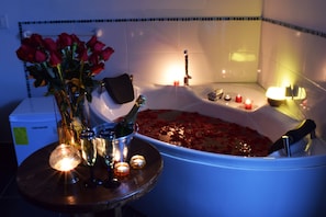 Une baignoire remplie de pétales de rose, un vase avec des roses rouges et des coupes à champagne sur une table.
