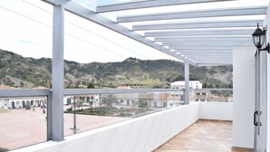 Un balcón con vistas a un paisaje montañoso, suelo de baldosas y barandilla blanca.
