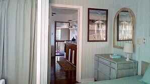 A bedroom with a bed, a dresser, a mirror, and a view of the kitchen through an open door. -   "The Most Convenient Location To Vacation" (Governor's Harbour)