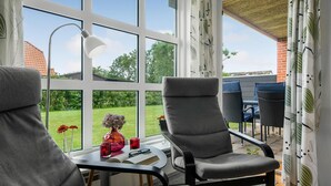 A conservatory with a view of a garden, a table with a chair, and a lamp.