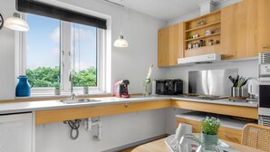 A modern kitchen with a window, stainless steel appliances, wooden cabinets, and a dining area with a table set for two.