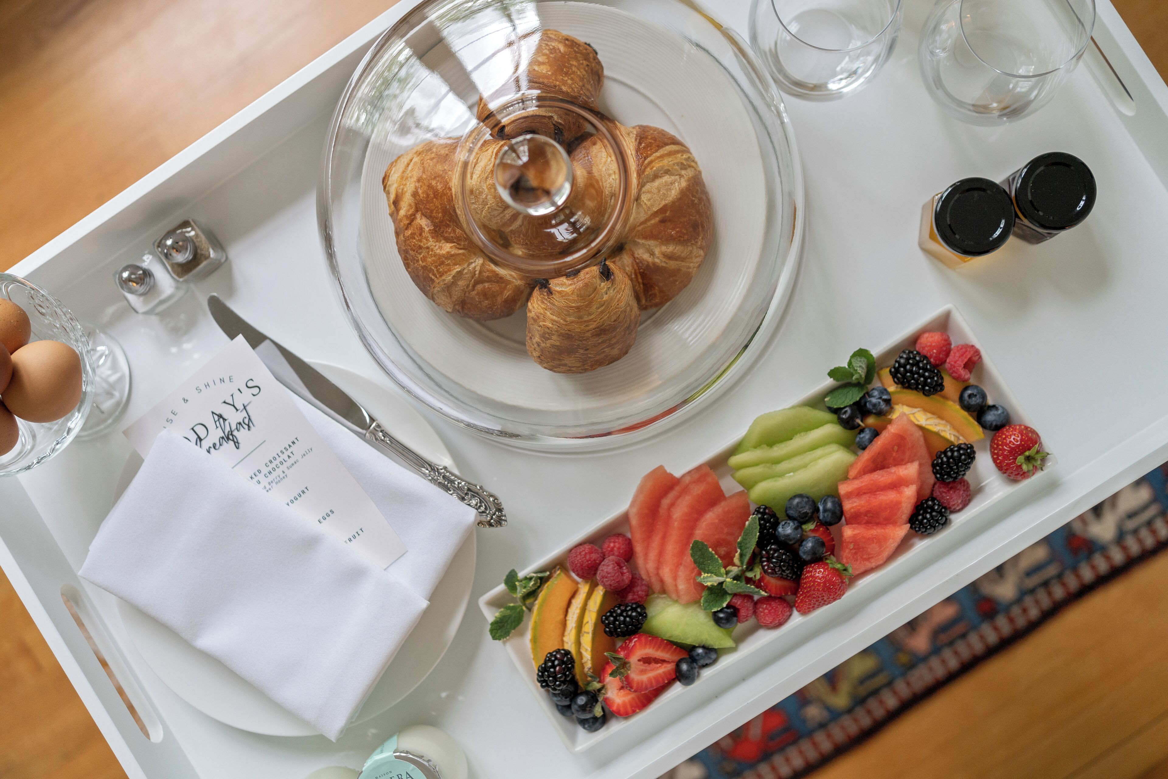 A breakfast tray with croissants, a fruit platter, a napkin, and a menu.