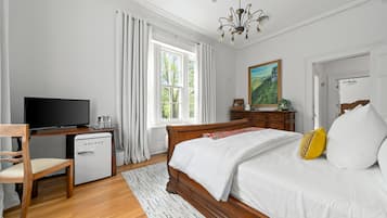 Ett sovrum med en säng, ett skrivbord med en tv, ett litet kylskåp och ett fönster med gardiner.