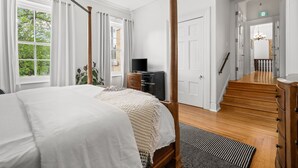 A bedroom with a large bed, a dresser, a television, and a staircase leading to another room. - The CAPE (Prince Edward)