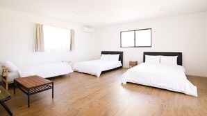 Een hotelkamer met drie bedden, een houten tafel en een raam met gordijnen.
