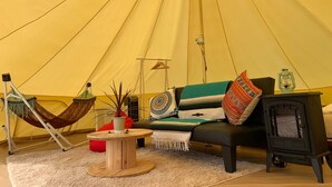 Een tent van binnen met een bank, een tafeltje, een hangmat en een houtkachel.